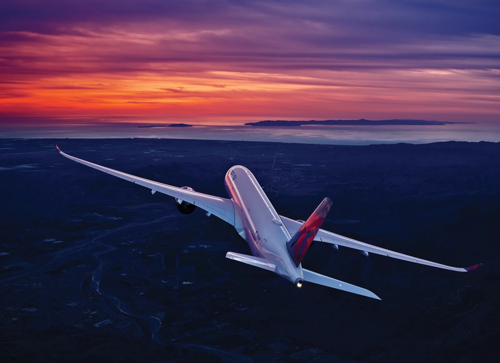 A Delta Air Lines Airbus A350-900 in flight at sunset over a coastline