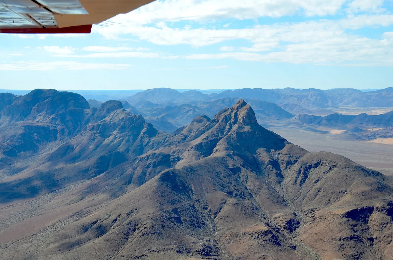 Aerial view of the Nubib Mountains on the eastern edge of the Namib, Namibia, with the wing of a light aircraft at the top left