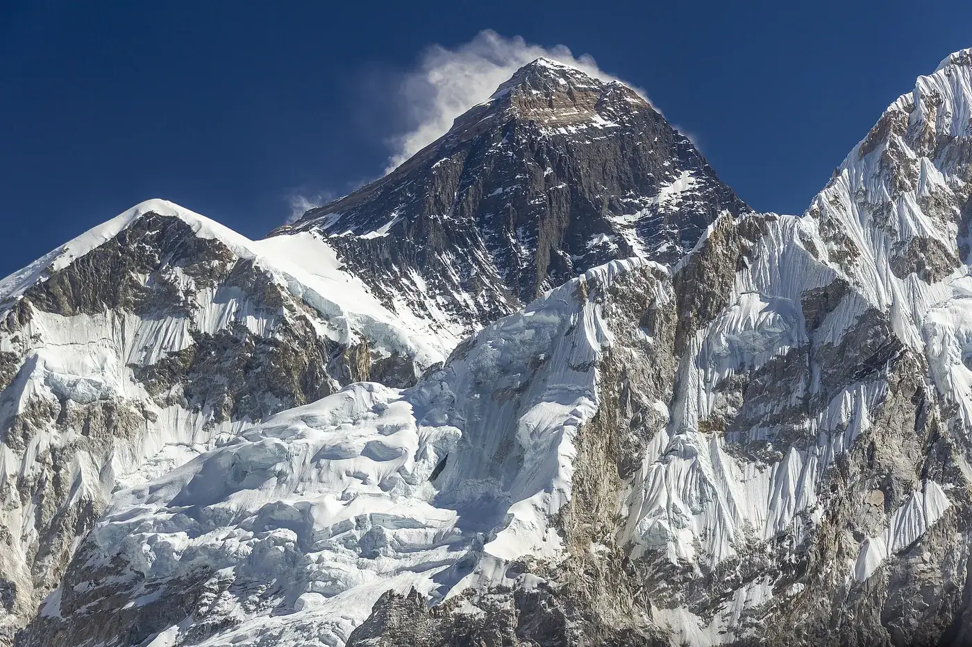 The dark summit pyramid of Mount Everest with a plume of cloud, above snow and ice ridges