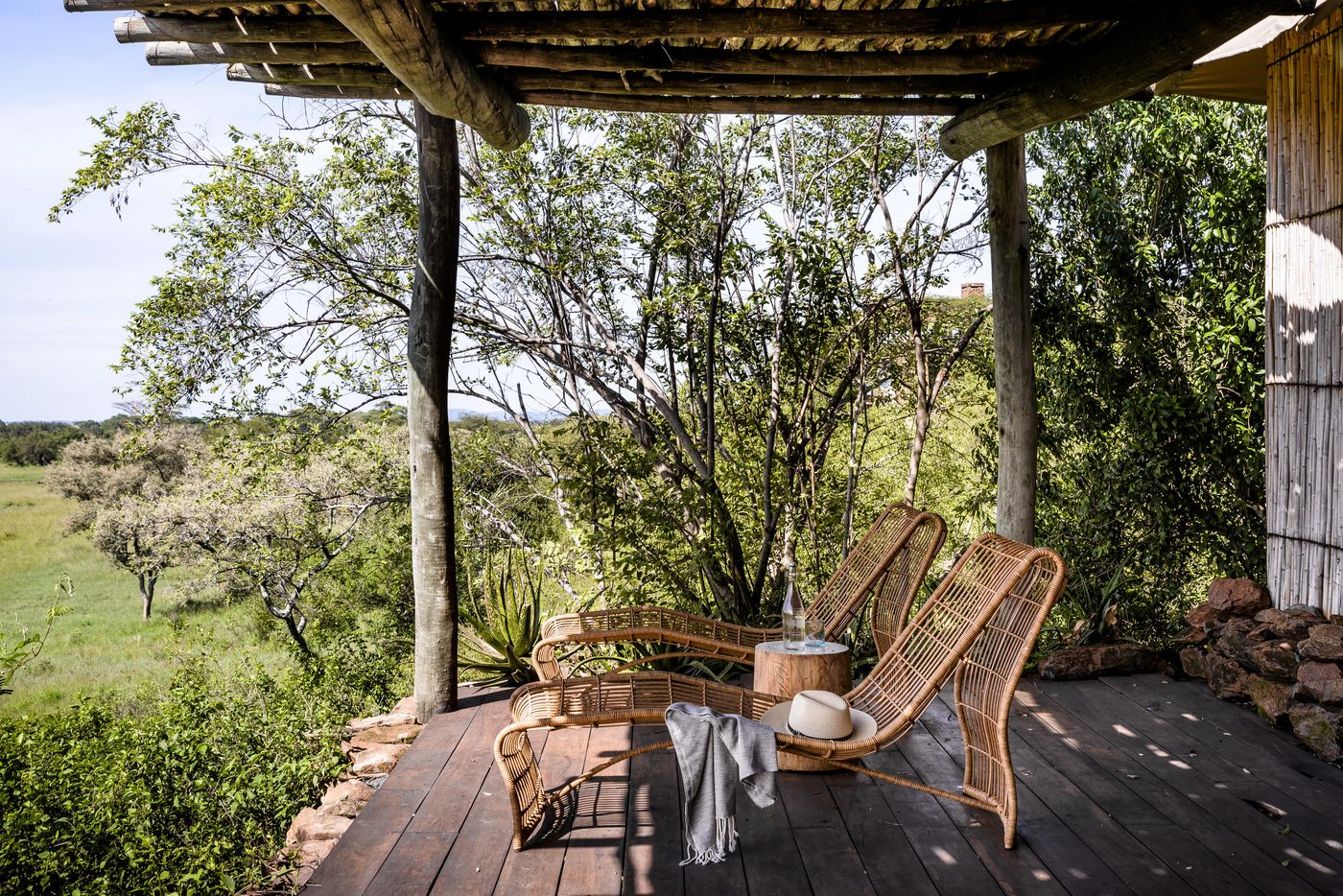 A wooden deck with two cane chairs under a thatched roof looking out over green bush at Singita Faru Faru, Tanzania