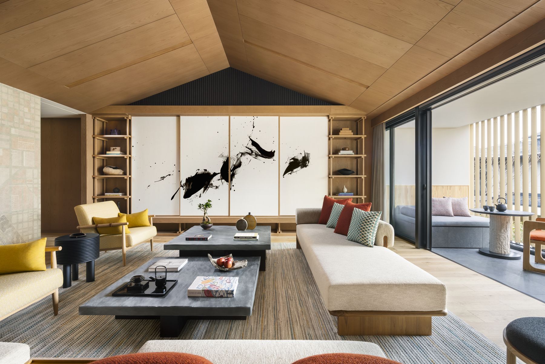 A long lounge with low sofas, a wooden ceiling, ink paintings on paper screens and glass doors to a terrace