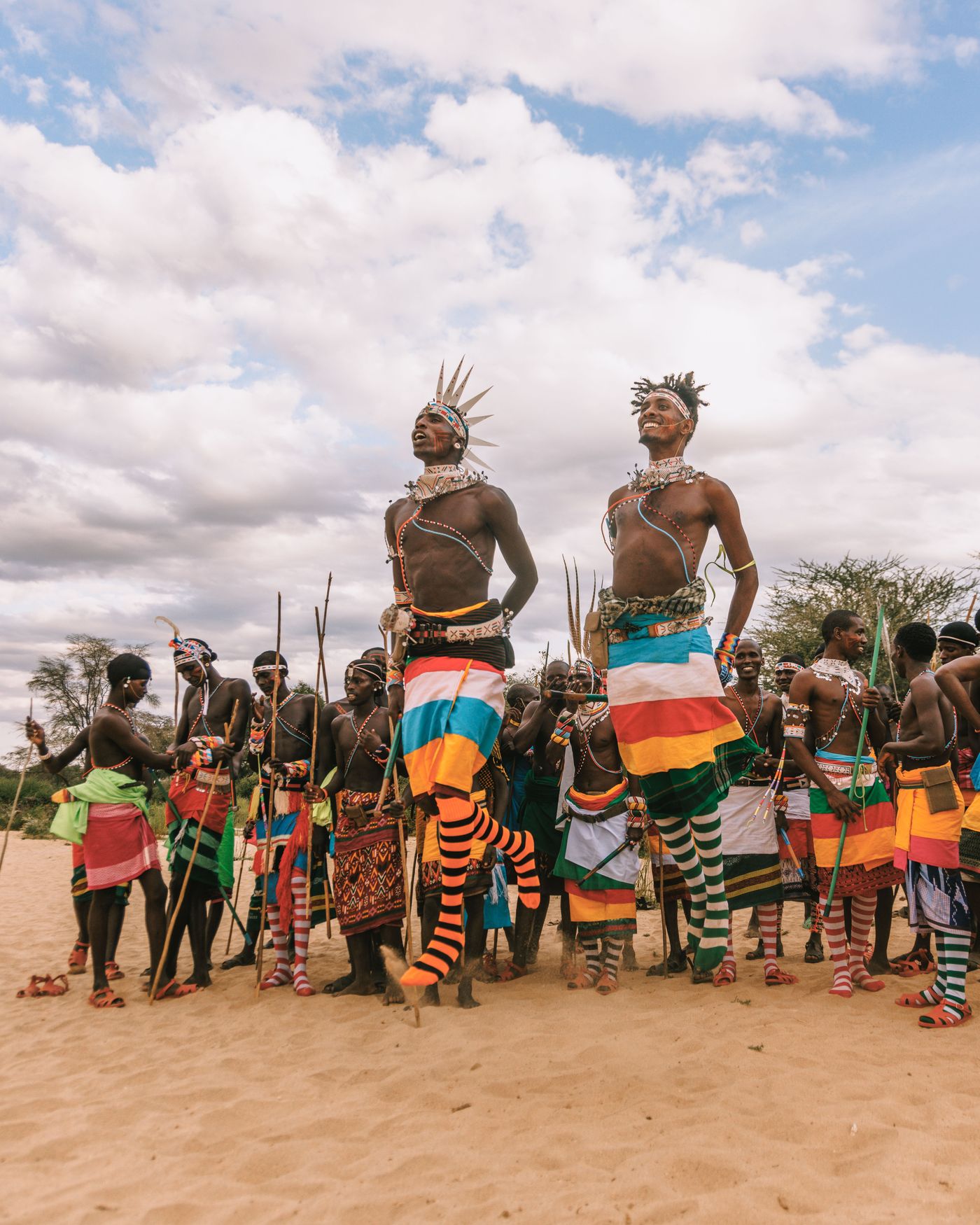Samburu warriors and women in red and white beadwork dancing in a line on sand at Kalepo Camp, Kenya