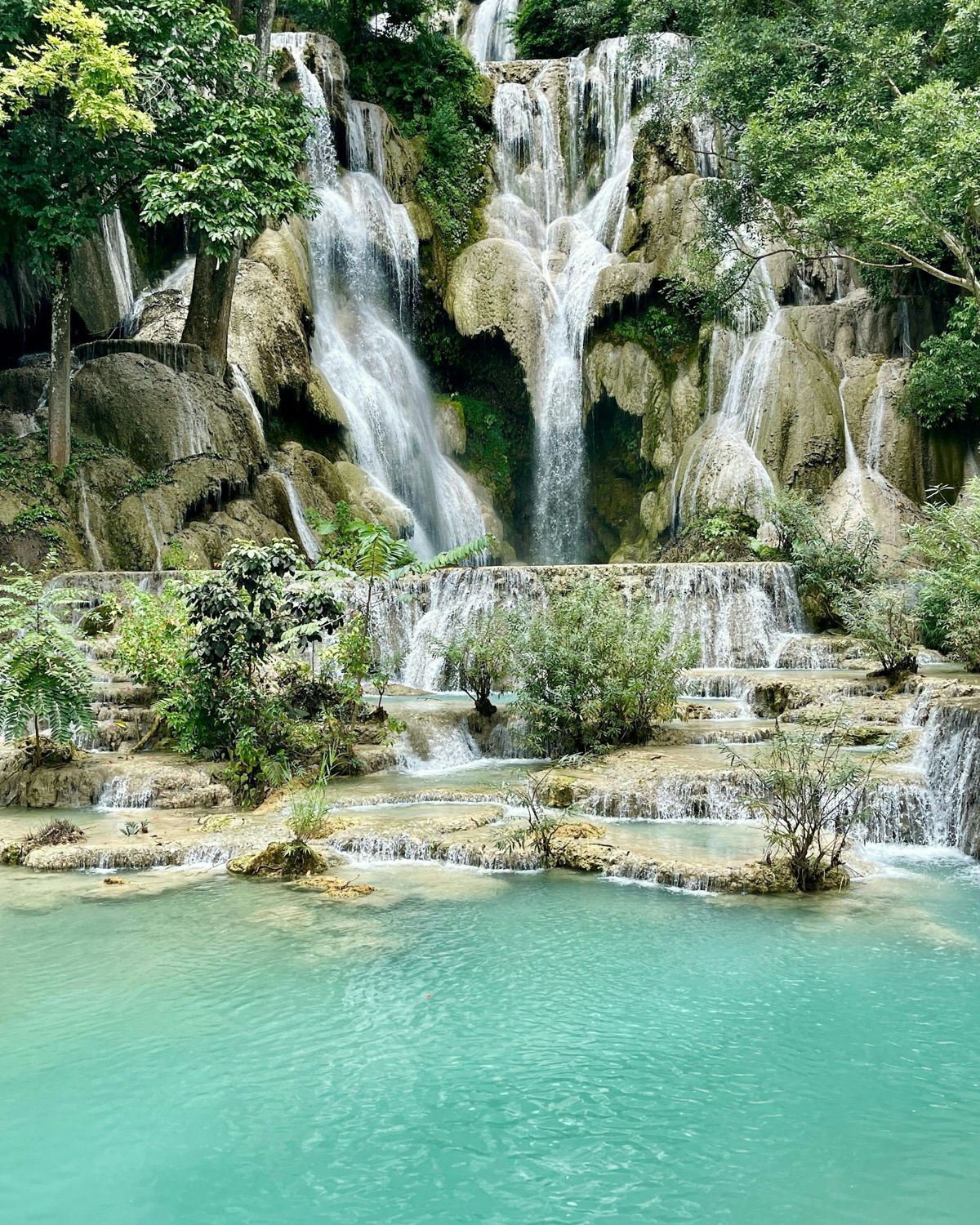 Water falling over pale limestone tiers into turquoise pools surrounded by forest at Kuang Si Falls, Laos