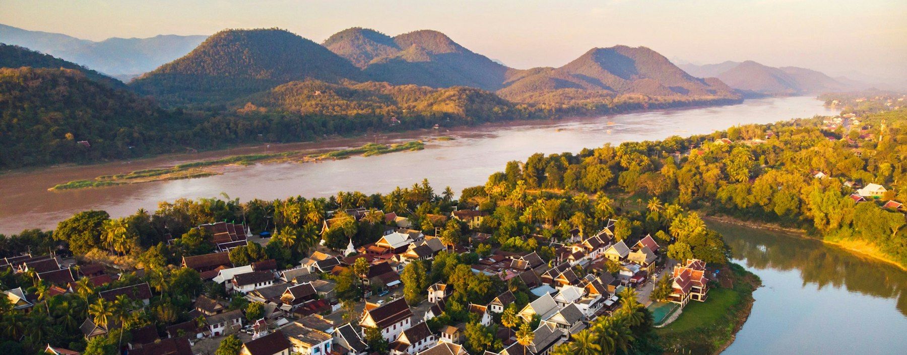 Luang Prabang from the hills, its roofs among trees beside a wide bend of the Mekong, with mountains beyond