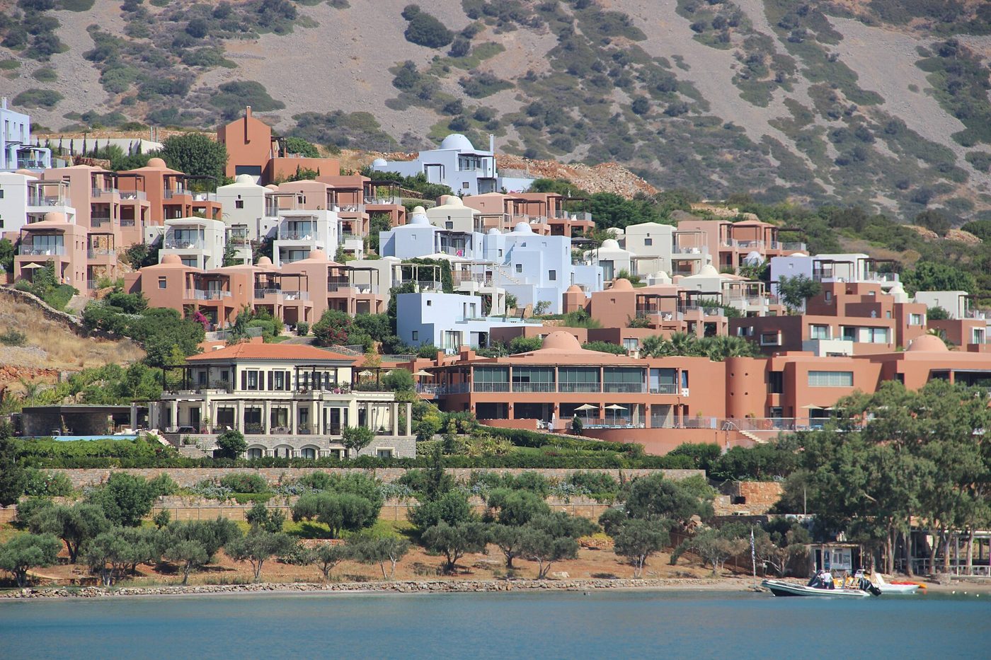 Terracotta and white villas of the Blue Palace resort stepping up a hillside above the bay at Elounda, Crete
