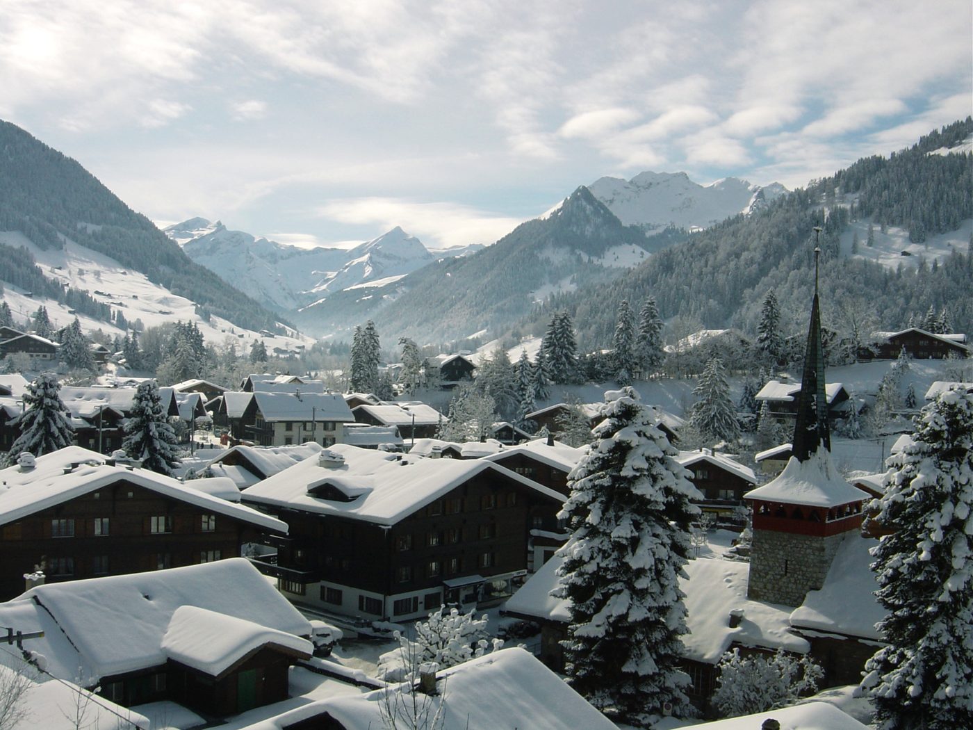 Snow-covered chalets and a church spire in Gstaad, with Alpine peaks behind