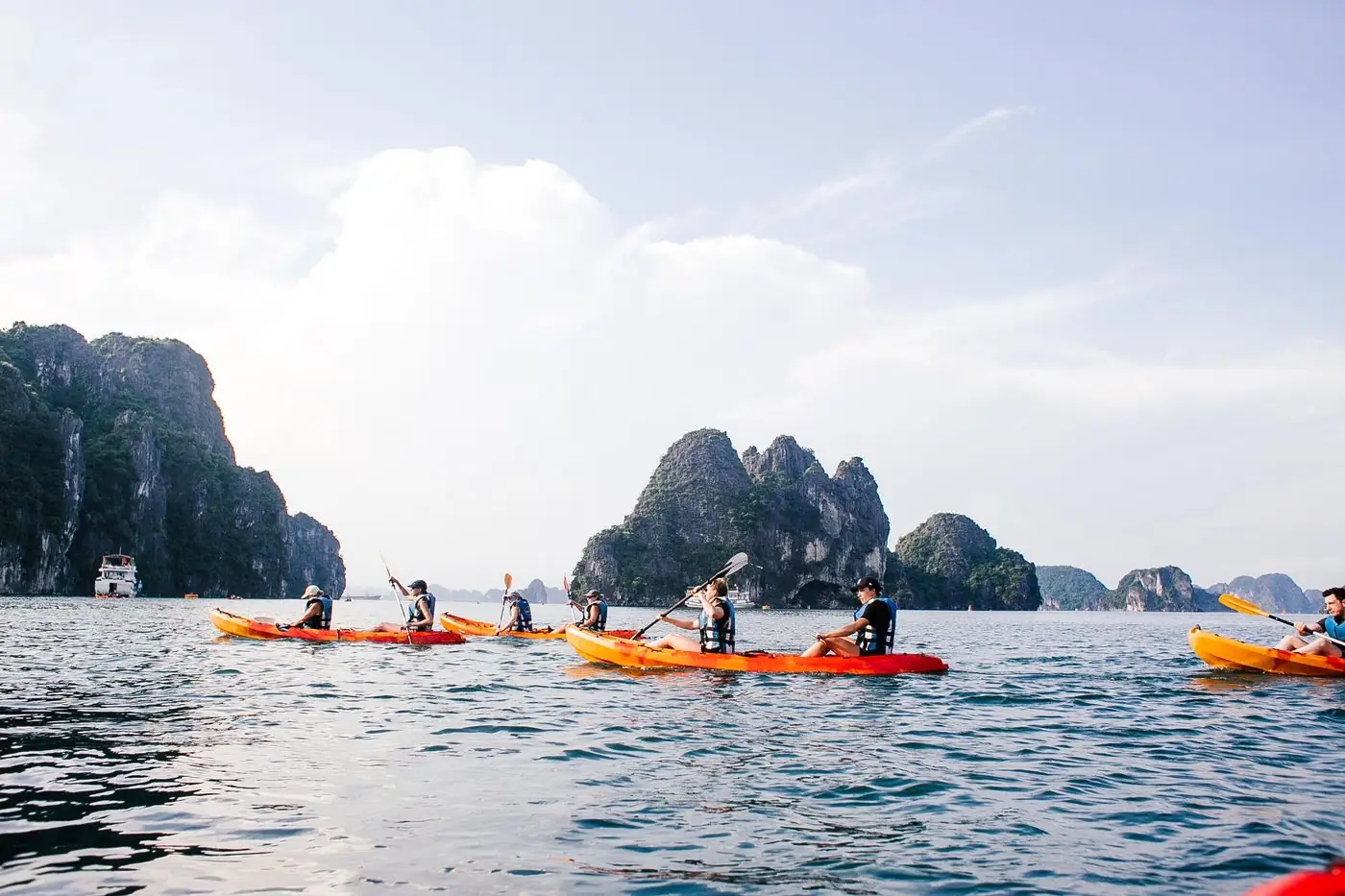 A line of people in orange and yellow sea kayaks paddling among limestone islands